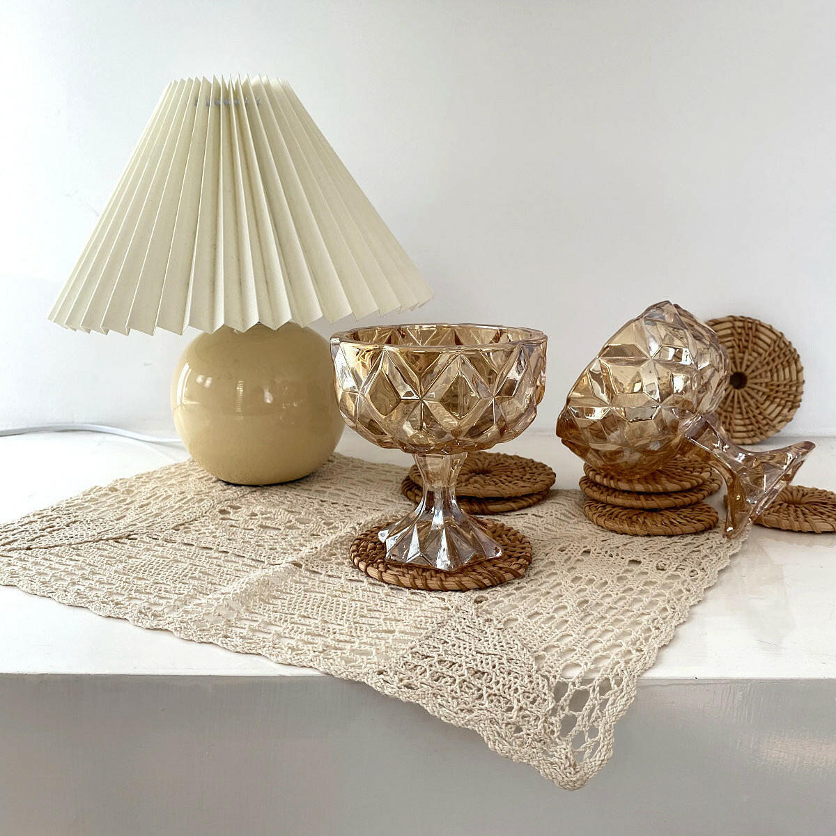 Vintage amber drinking glass featured with decorative lamp and woven coasters on a lace tablecloth