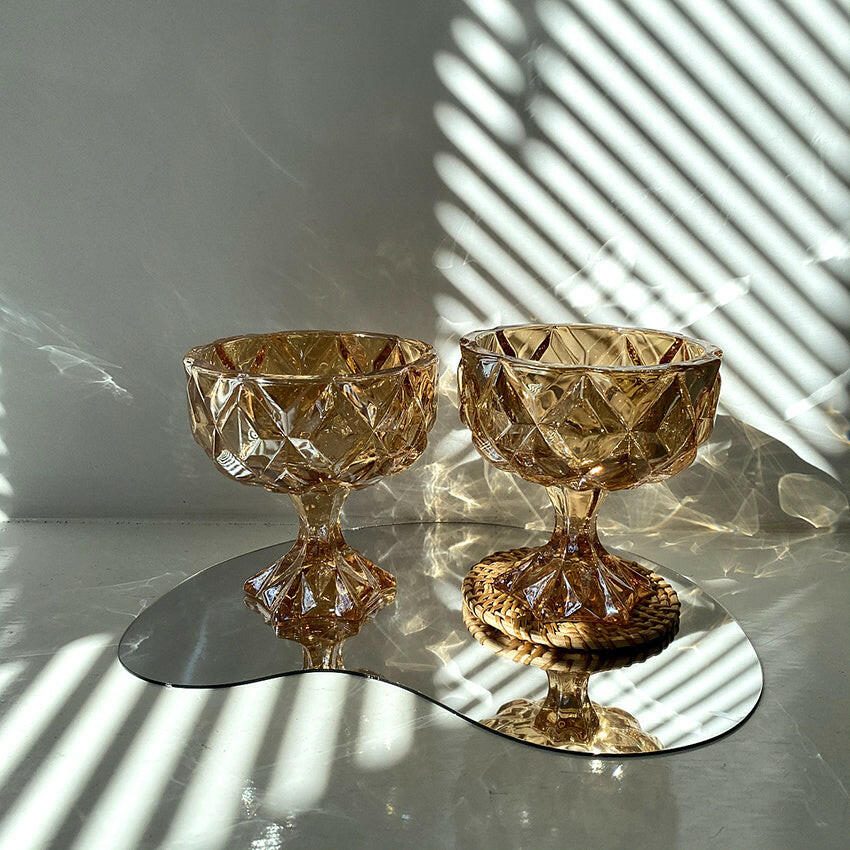 Set of two vintage amber drinking glasses with diamond-shaped cut designs on a reflective surface