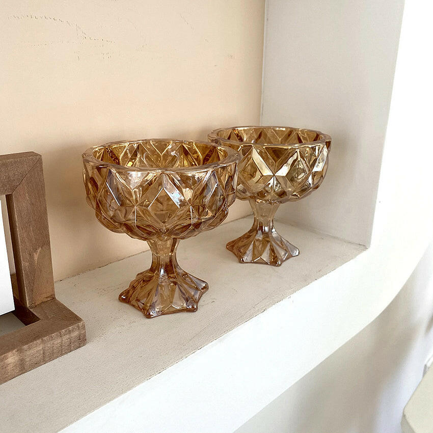 Two vintage amber drinking glass cups with a diamond pattern on a display shelf